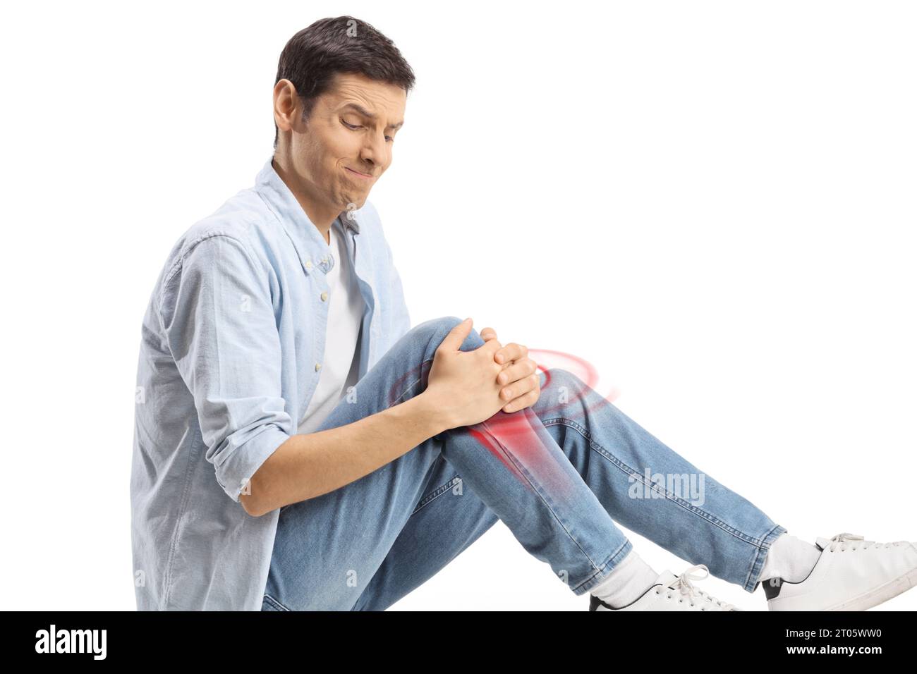 Young man sitting on the floor and holding his knee in pain, bone inflammation with red, isolated on white background Stock Photo