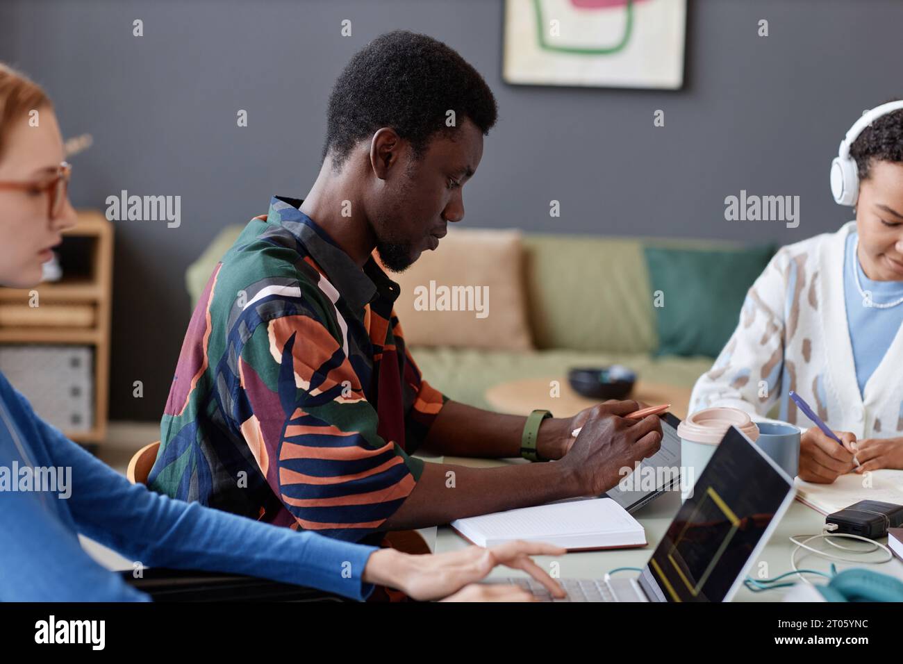Side view portrait of young Black man using digital tablet while working with team at table, copy space Stock Photo