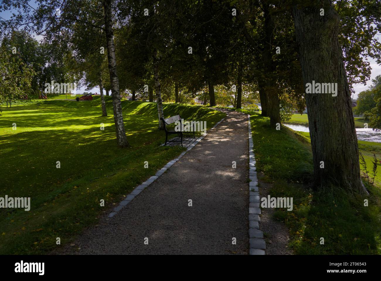 A curved paved path if the shadow of trees. Stock Photo