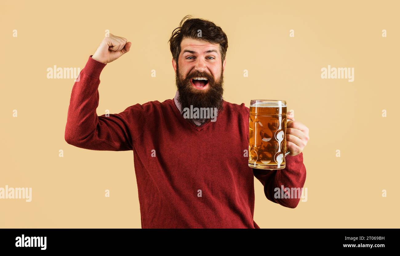 Happy man drinking craft beer and celebrating victory at bar. Handsome male with mug beer making winning gesture with raised arm. Success. Bearded man Stock Photo