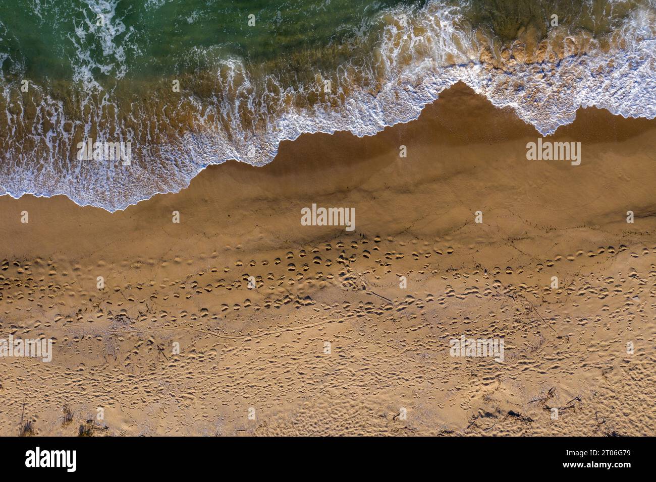 Aerial view of a remote sandy beach with foot steps and sea waves by drone Stock Photo