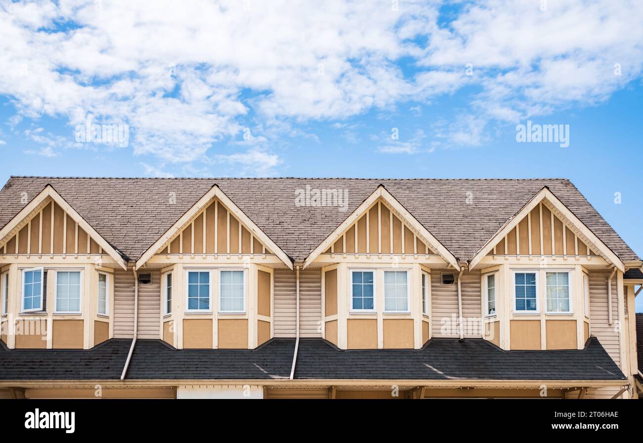 The roof of the house with nice window. Houses with shingle roof against blue sky. Edge of roof shingles on top of the houses dark asphalt tiles on th Stock Photo