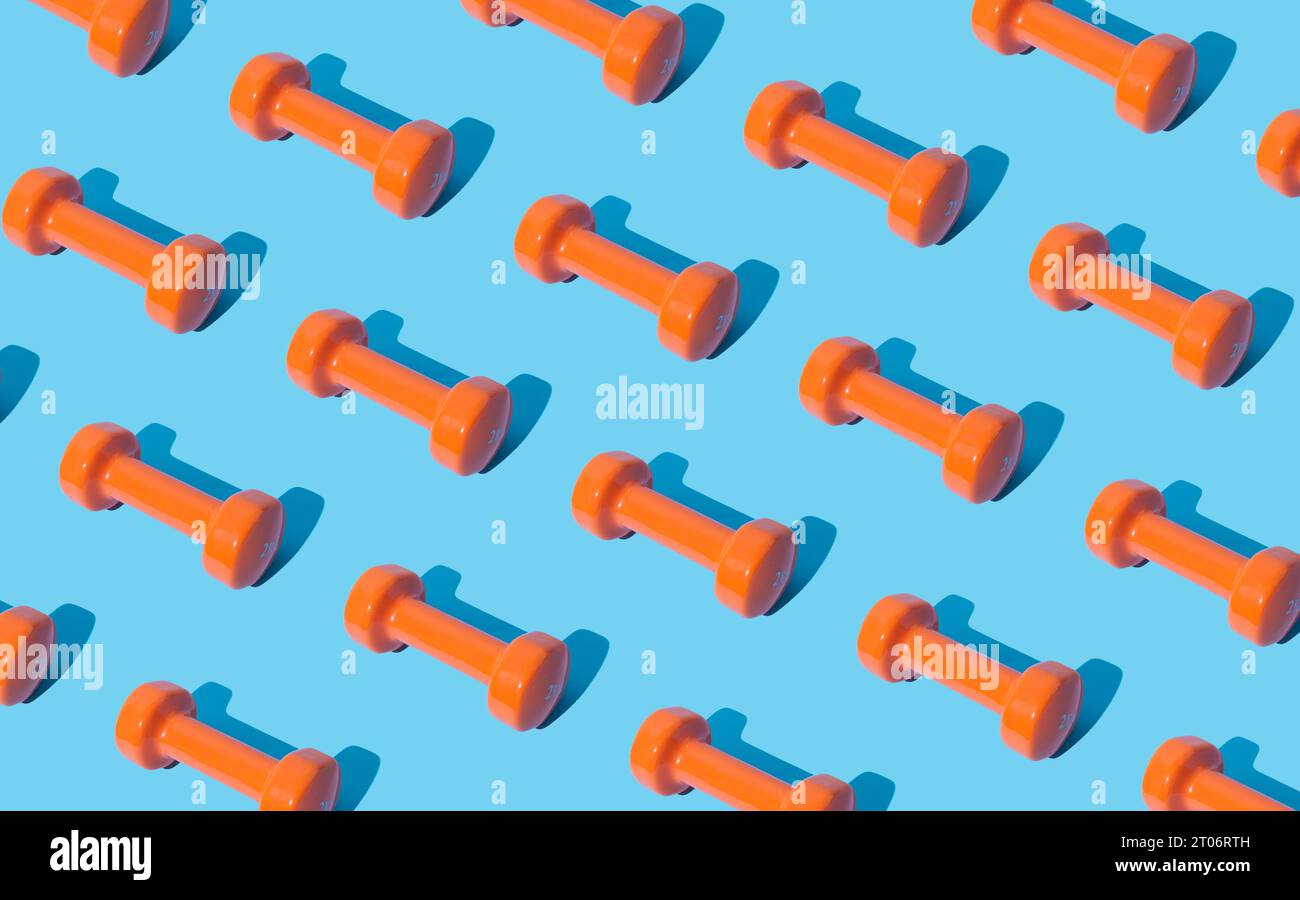 Creative pattern composition made of orange dumbbells on light blue background. Minimal fitness, healthy lifestyle and sport concept. Stock Photo