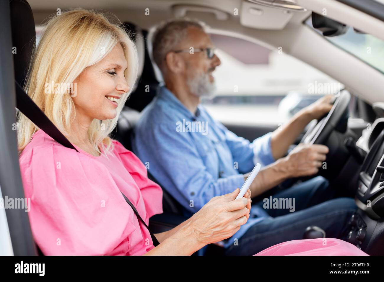 Happy elderly woman using smartphone while riding car with husband Stock Photo
