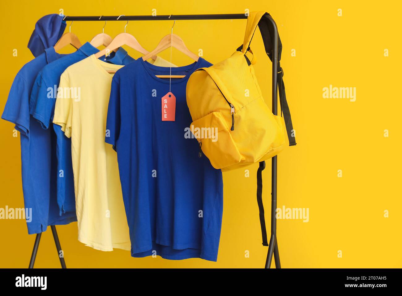 Rack with t-shirts, cap and backpack on yellow background. Black Friday sale Stock Photo