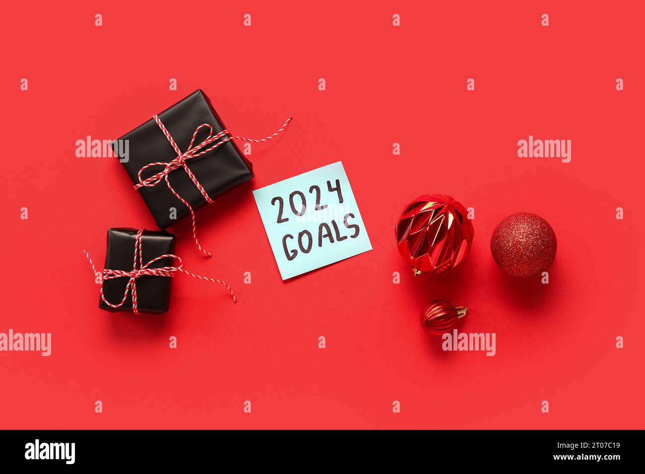 Sticky note with goals for 2024, gift boxes and Christmas balls on red background Stock Photo