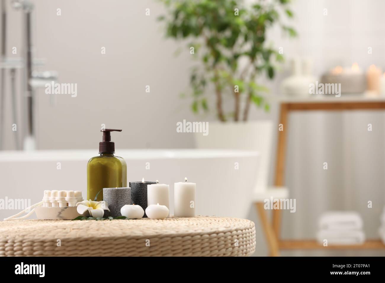 Spa products, burning candles and plumeria flower on wicker table in ...