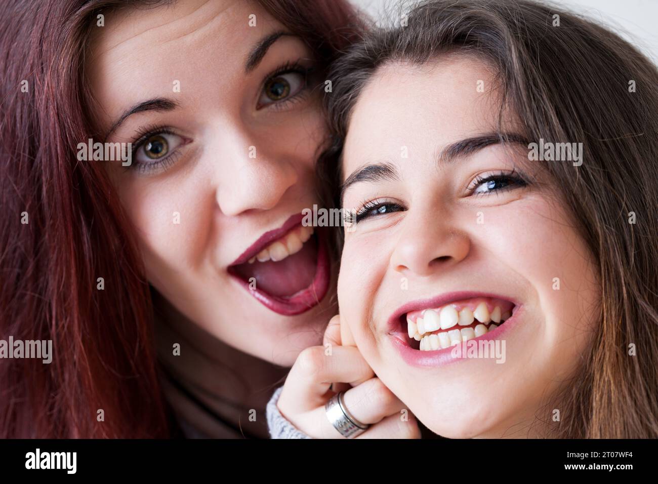 Two young women with meticulous makeup and long hair make goofy faces for selfies. Exuding joy and carefreeness, they playfully experiment with expres Stock Photo