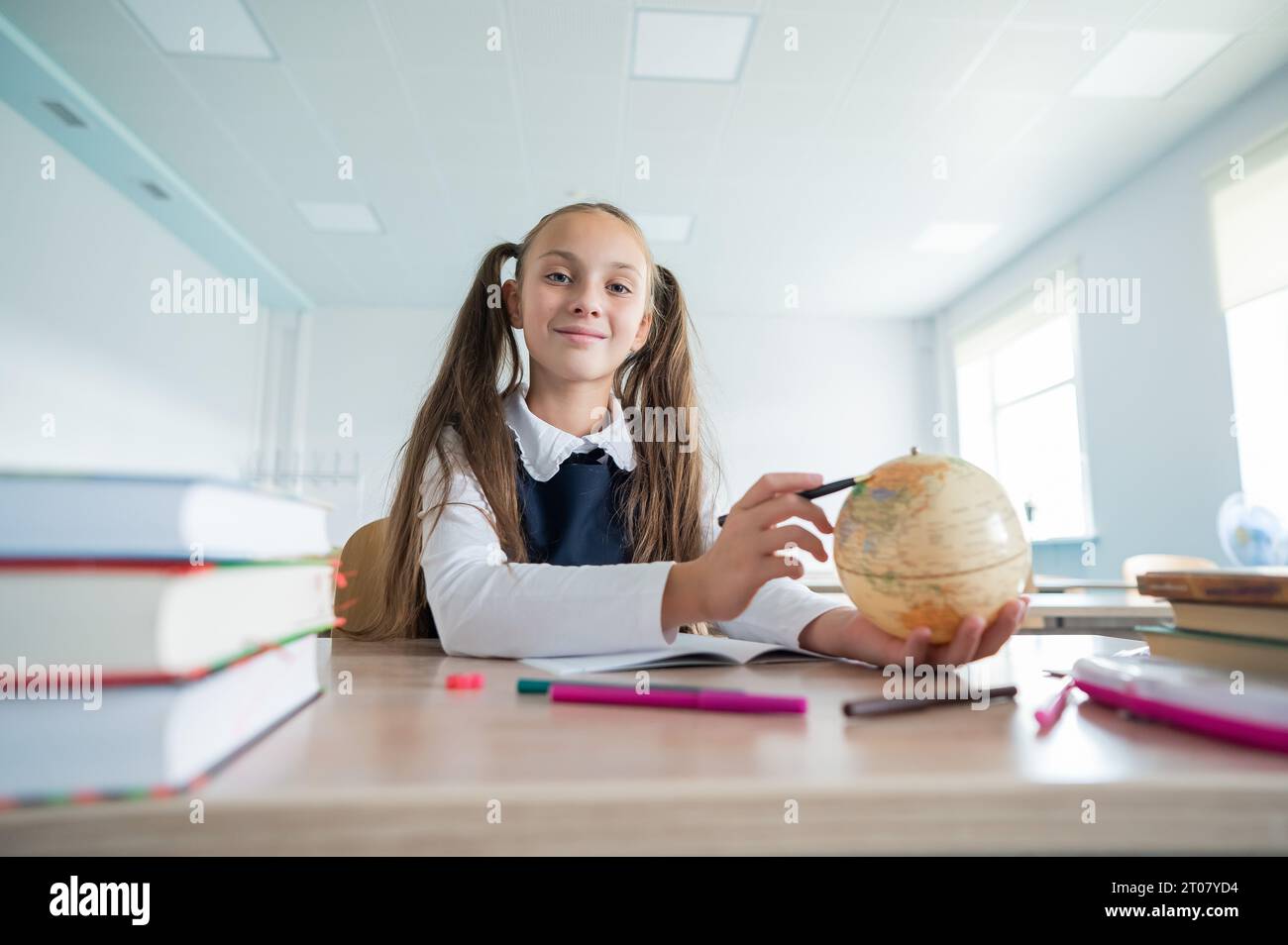 Caucasian schoolgirl sits at her desk at school and studies the globe ...