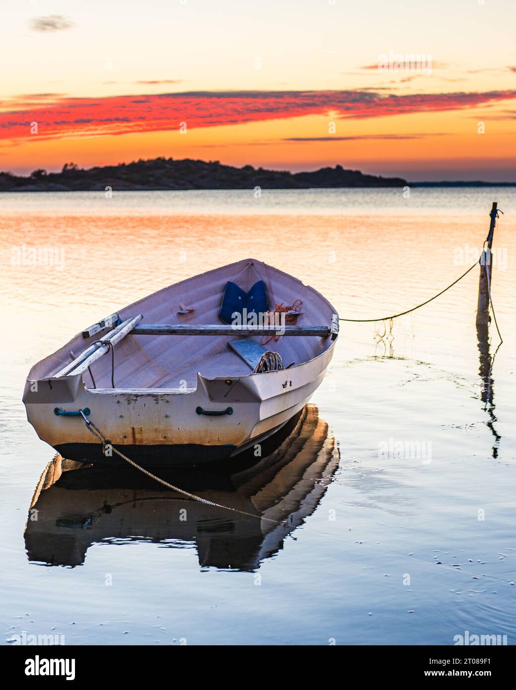 Moored nautical vessel at sunset, reflecting on calm ocean water. Stock Photo