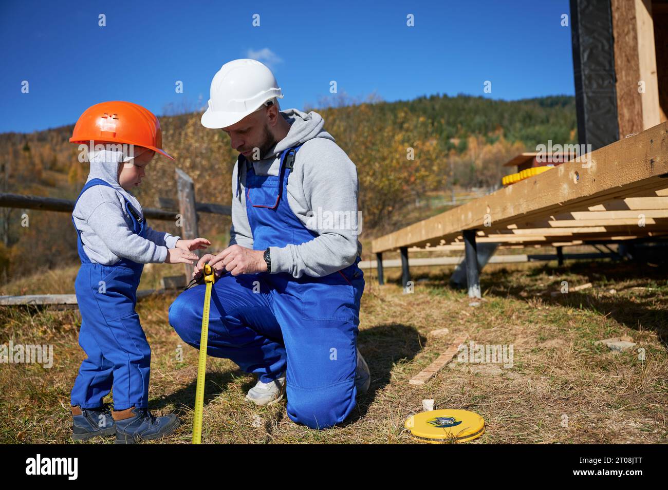 Contruction Project Parents Father with toddler son building wooden frame house on pile foundation ...