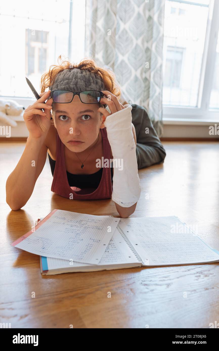 Teenage girl with broken arm in cast, wearing glasses, doing homework ...