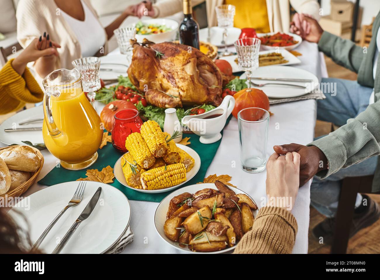 cropped view multiethnic family praying together at festive table with turkey and wine, Thanksgiving Stock Photo