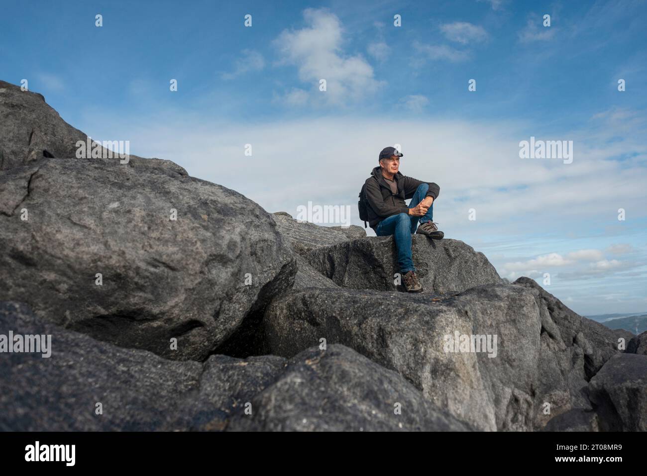 Male backpacker sitting on rocks enjoying the view after walking up a mountain Stock Photo