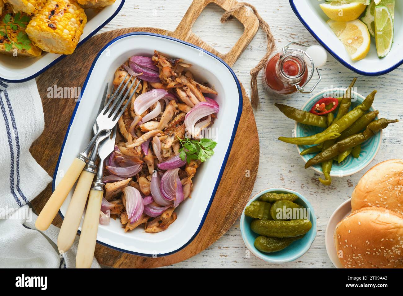 Pulled bbq chicken with baked onions on serving platter, bbq corn, pickles, chili peppers and buns for hot dogs and burgers, tomato sauce. Traditional Stock Photo