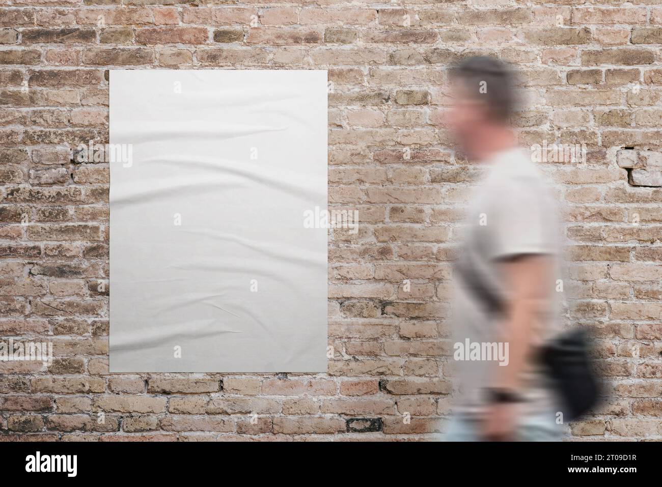 Wrinkled, blank A3 poster in white, adhered to a brick wall. A man walks beside. Ad or marketing campaign design promotion Stock Photo