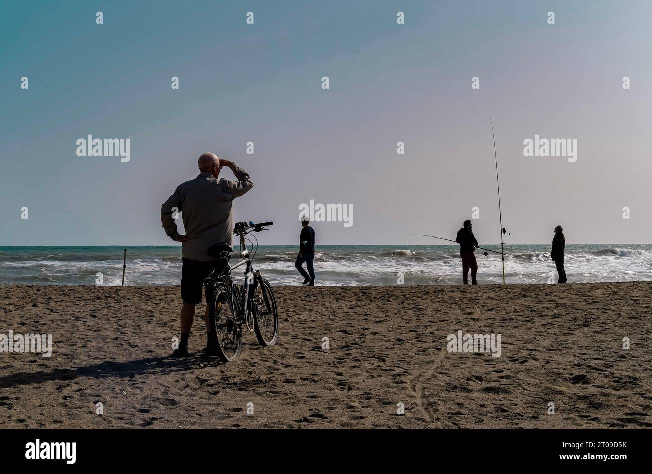 Man looking at the shore with his hand on his forehead to protect himself from the sun, with his bicycle Stock Photo