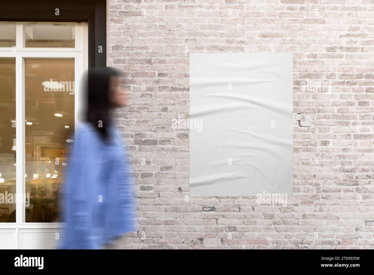 Poster adhered to a brick wall next to a shop door. Woman in motion walking beside. The urban scene with dynamic movement for poster mockup and design Stock Photo