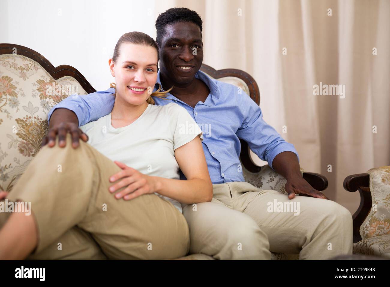 Portrait of positive wife and husband sitting on sofa in apartment