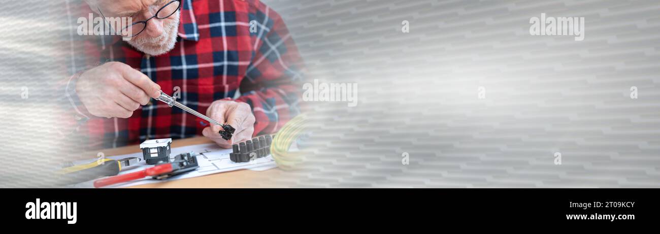 Senior electrician connecting wires in terminal block; panoramic banner Stock Photo