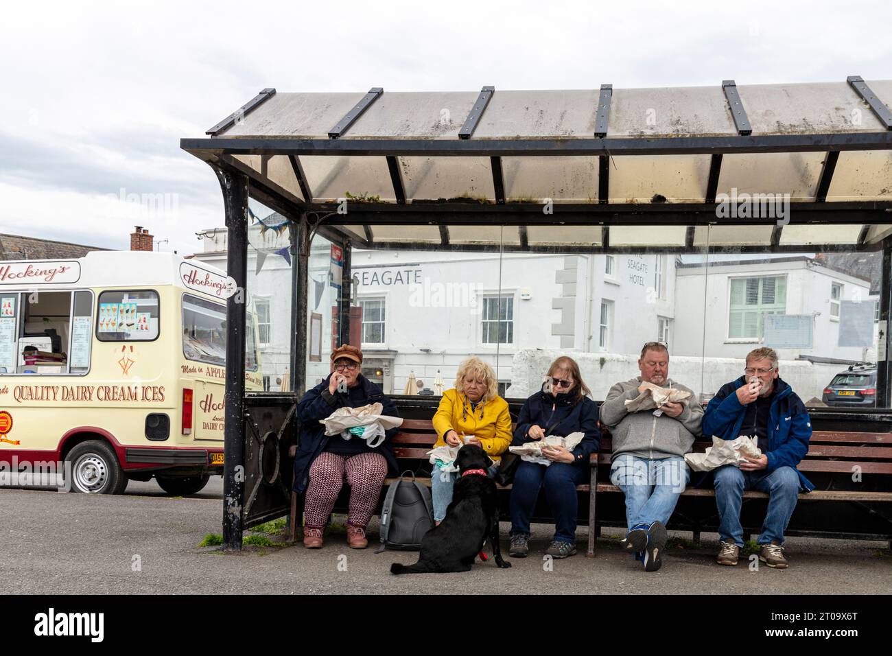 fish and chips, eating fish and chips, eating outside,  fat people, obese, obesity, eating fish and chips out of paper, al fresco, bus shelter Stock Photo