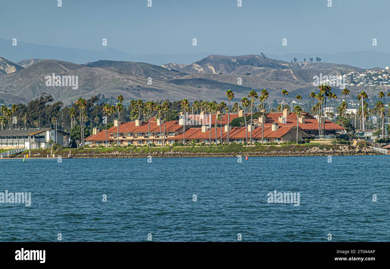 Ventura, CA, USA - September 14, 2023: Ventura Harbor Village Shopping Center building with red roof behind blue ocean water. Green palm trees, blue s Stock Photo