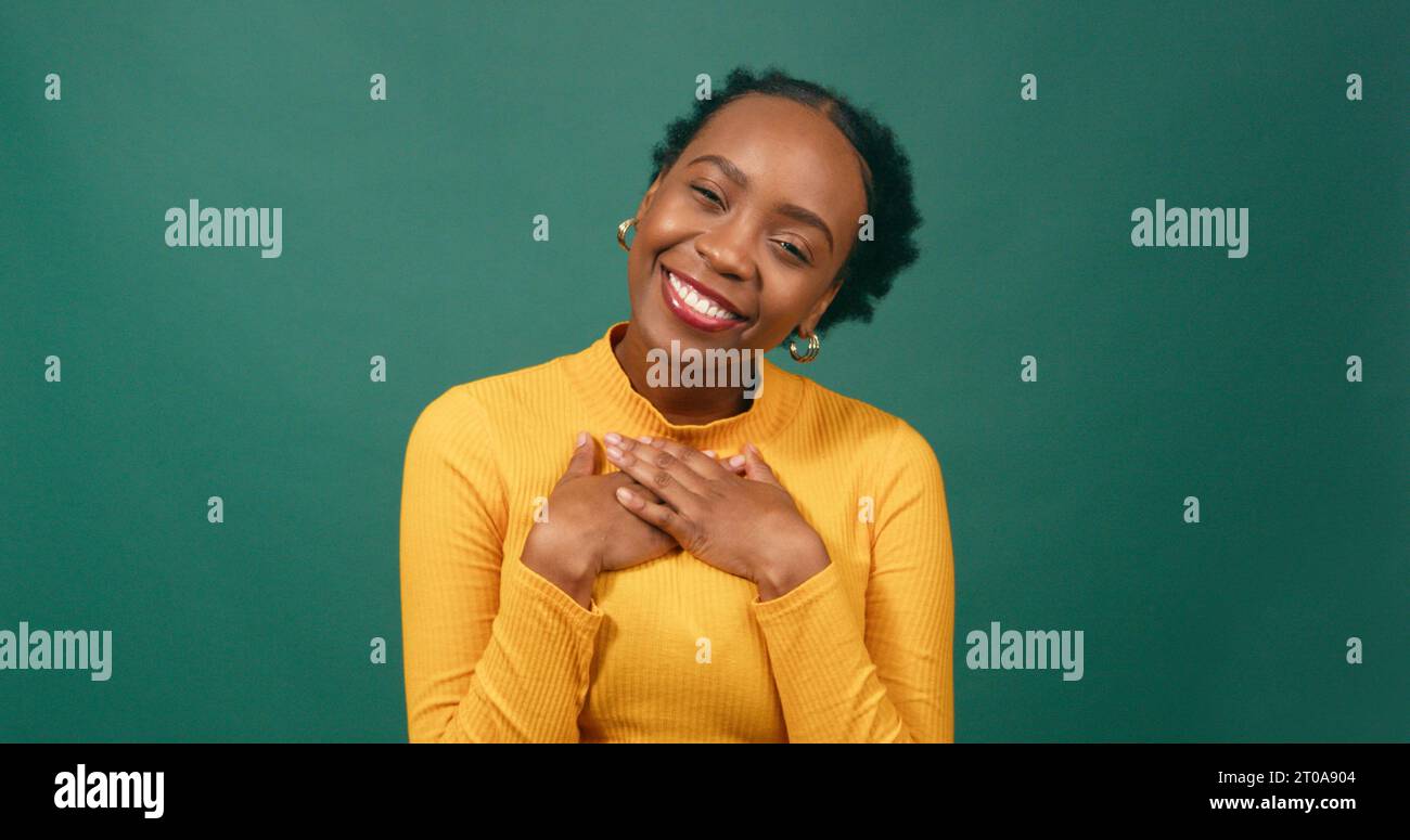 Beautiful woman puts hands on heart, infatuated and dreaming of crush, studio Stock Photo