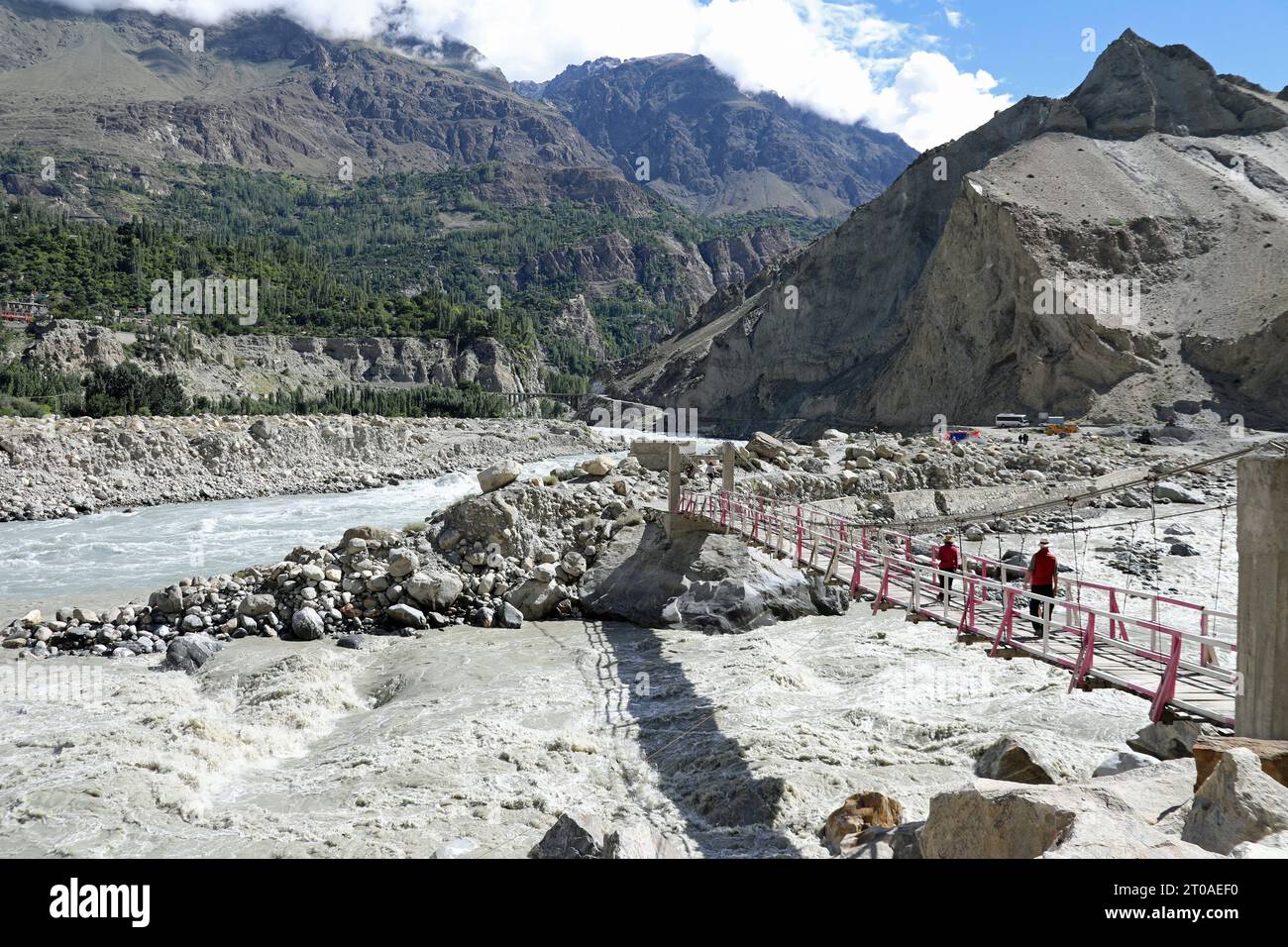 Tourists crossing a bridge over the Nagar River at its confluence with the Hunza River in Pakistan Stock Photo
