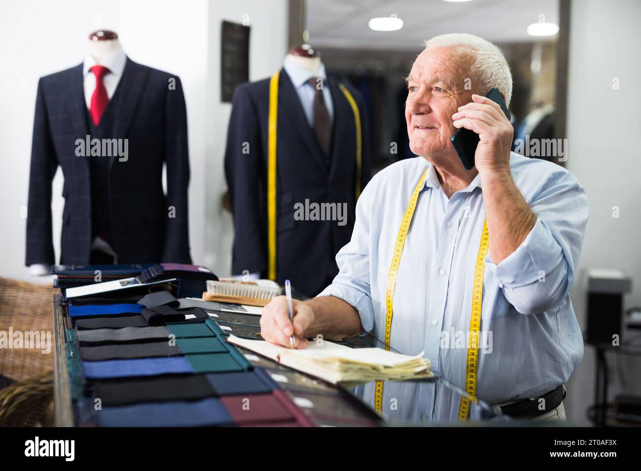Professional tailor man talking on mobile phone and making notes in notebook Stock Photo