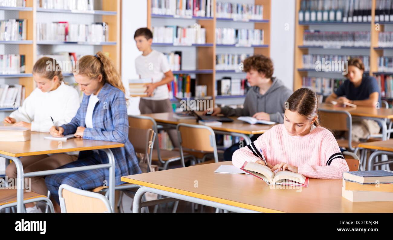 Portrait of preteen girl reading books in college library Stock Photo ...