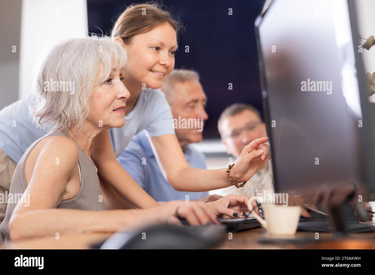 Old woman learning computer programs with teacher in training room Stock Photo