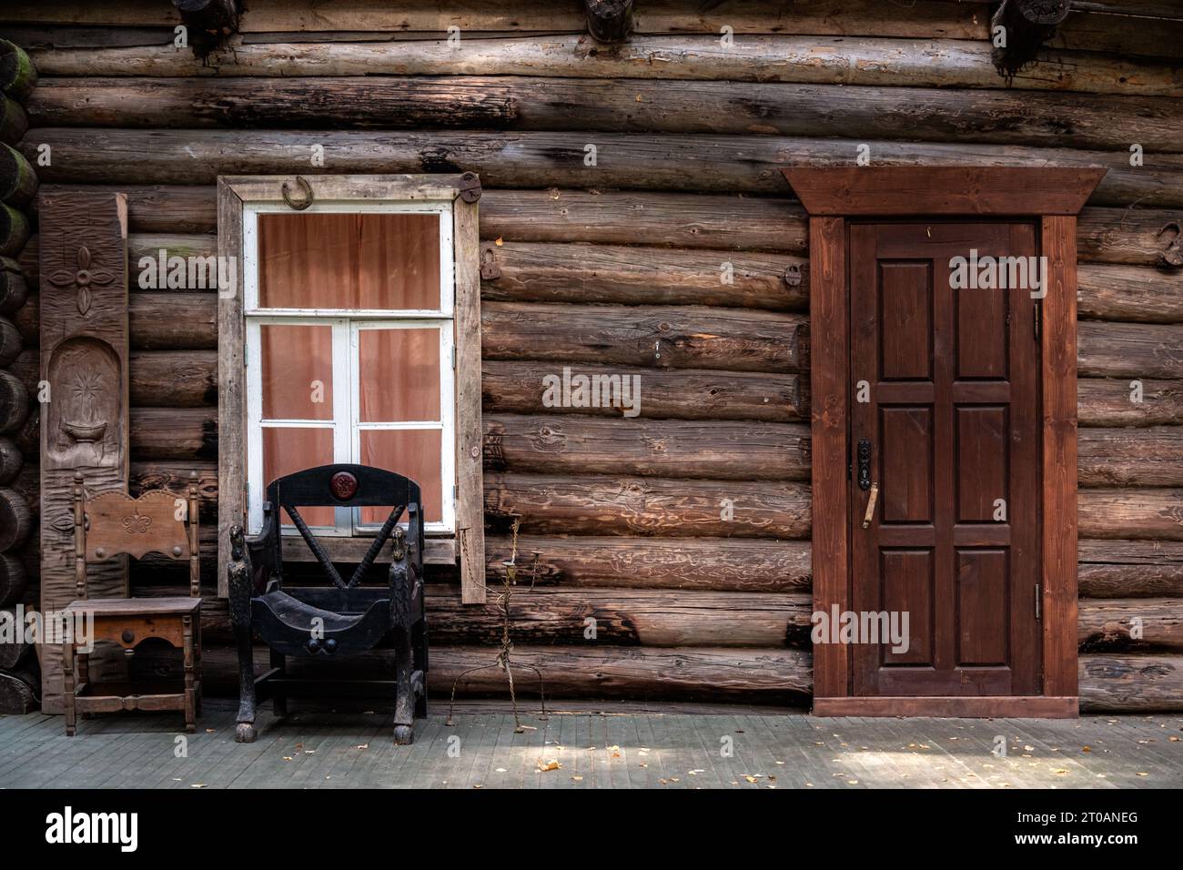 Fragment of a log house with a rectangular window in a white frame, a wooden door and a leather chair. Stock Photo