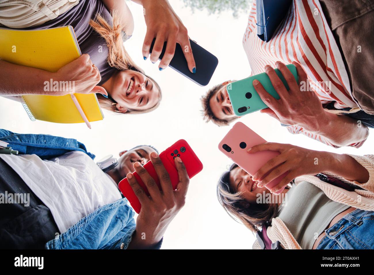 Low angle view of multiracial group of young adult friends enjoying and  smiling using their cellphone app. Portrait of a students hands holding a  smart phone. Colleagues sharing with mobile phones. High