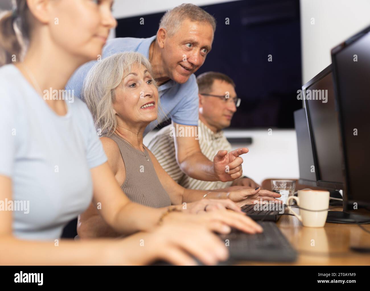 Old woman learning computer programs with teacher in training room Stock Photo