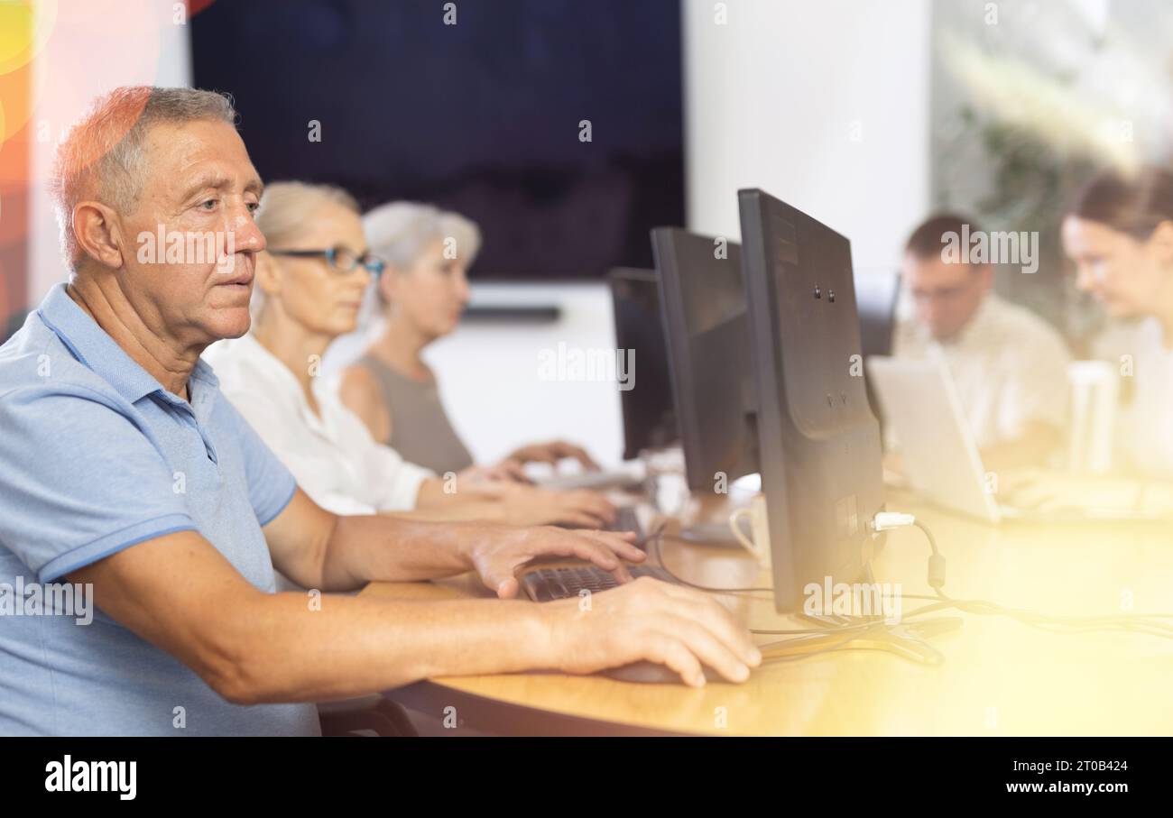 Focused older gentleman using computer at internet cafe Stock Photo