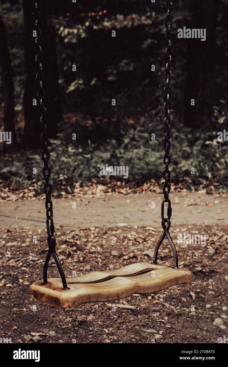 Empty swing on the playground. Old abandoned playground in the forest. Spooky quiet place. Horror swings without children. Autumn depression concept. Stock Photo
