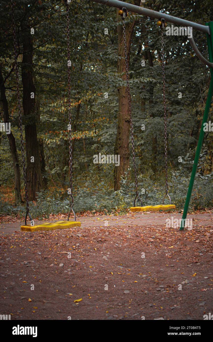 Empty swing on the playground. Old abandoned playground in the forest. Spooky quiet place. Horror swings without children. Autumn depression concept. Stock Photo