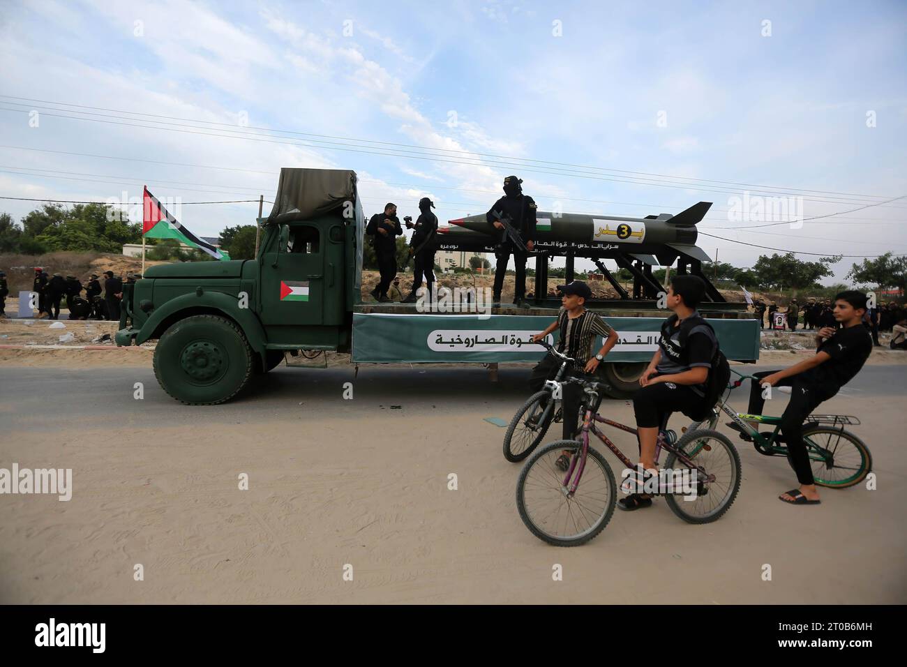 Palestinian children watch members of the Al-Quds Brigades, the military wing of the Islamic Jihad movement, participating in an anti-Israel military parade on the occasion of the 36th anniversary of the founding of the movement in Gaza City. Stock Photo