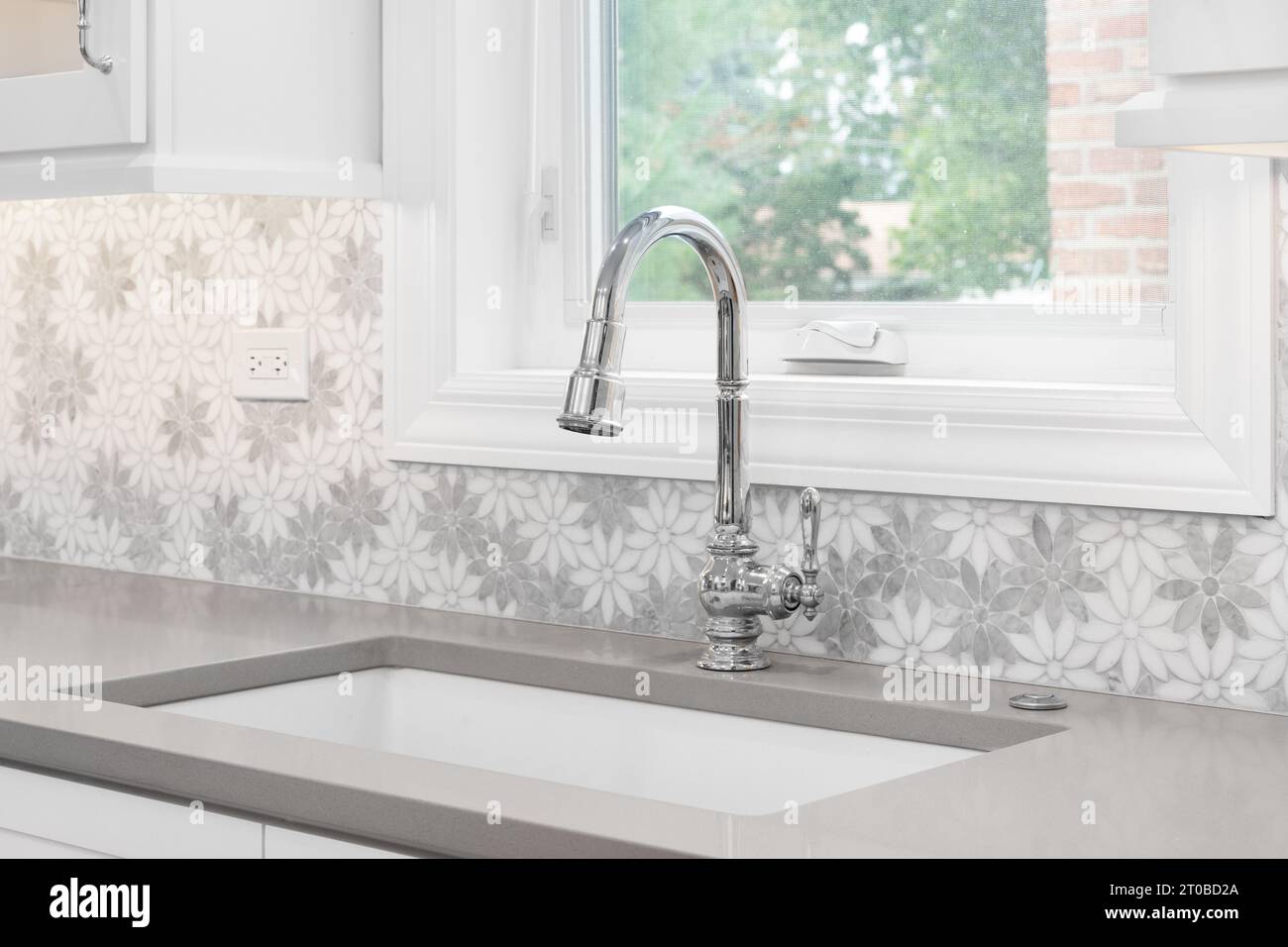 A kitchen faucet detail with a marble daisy flower tiled backsplash, white chrome