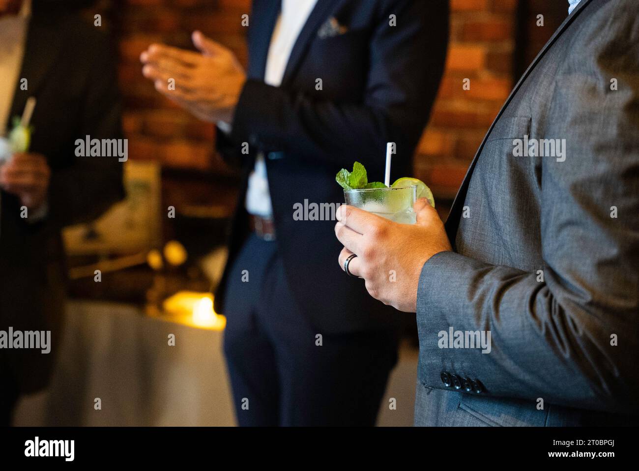 Close up of mojito cocktail in man hand in a business suit with blurred people in the background on the business event party. Stock Photo