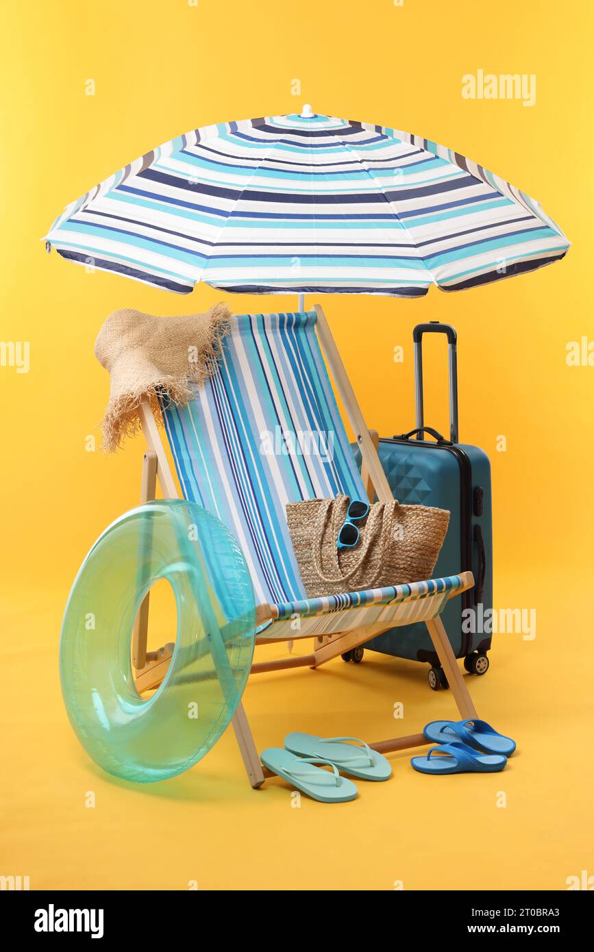 Deck chair, umbrella, suitcase and beach accessories on yellow ...