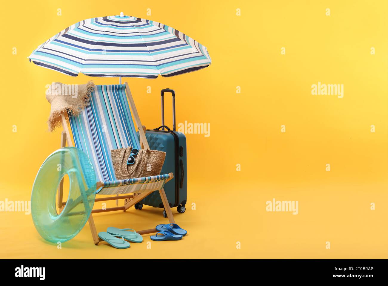 Deck chair, umbrella, suitcase and beach accessories on yellow ...