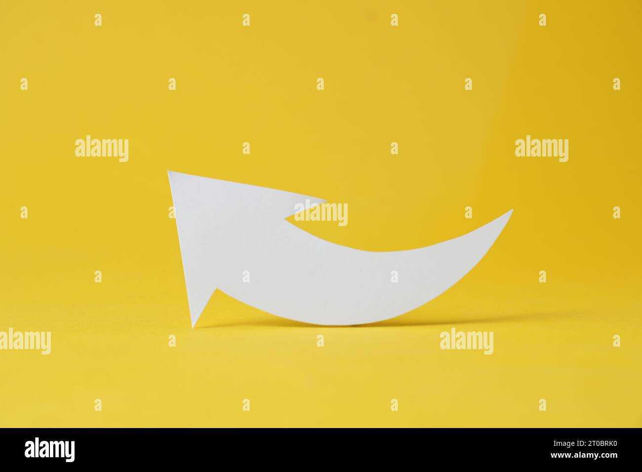 White curved paper arrow on yellow background Stock Photo