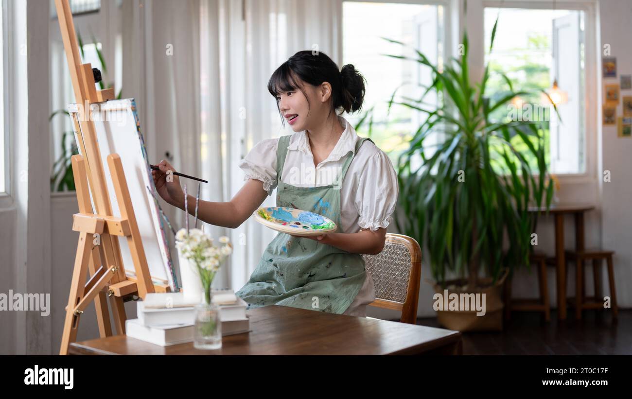 A beautiful and talented young Asian female artist painting on a canvas ...