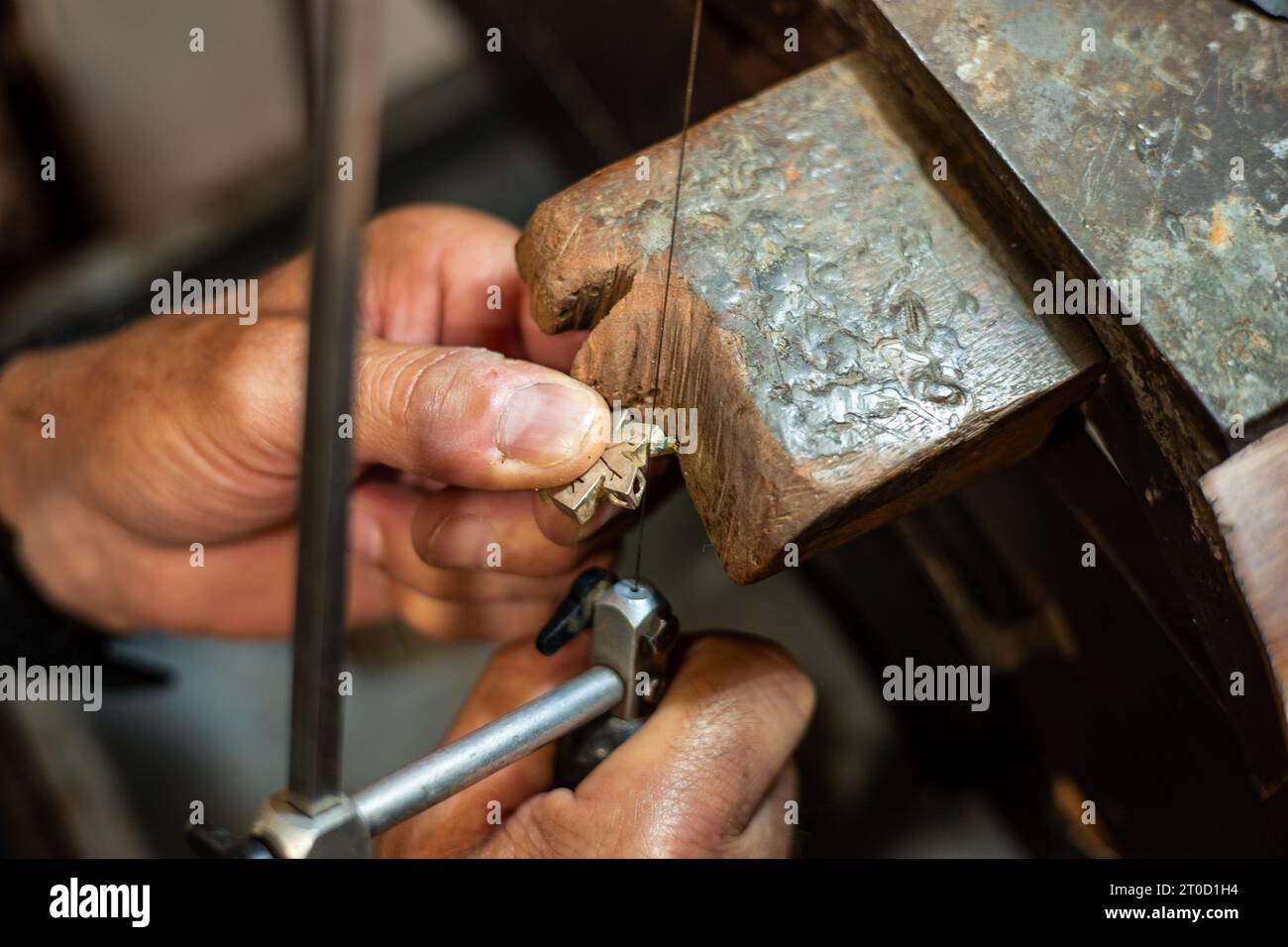Goldsmith working and creating in his crafting gold jewelry workshop. Jeweler sawing a silver jewel. Stock Photo