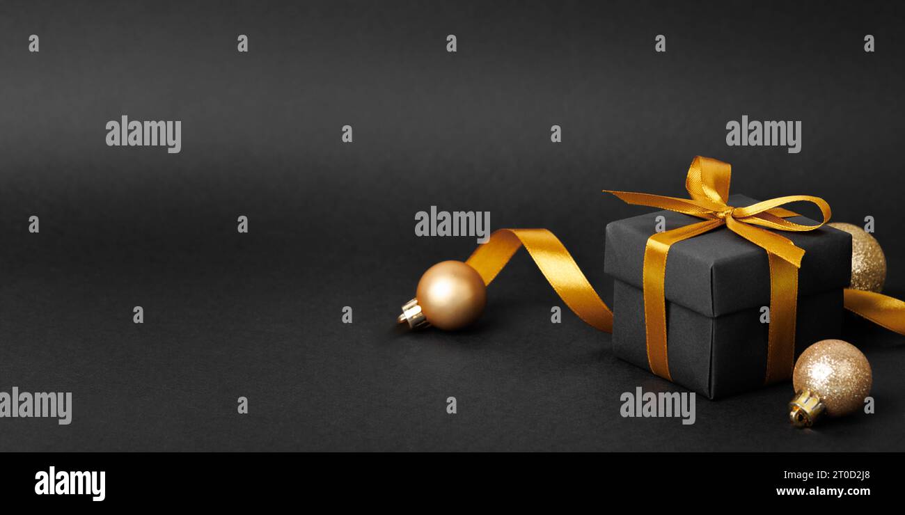 Black gift box with golden ribbon bow on black background. Stock Photo