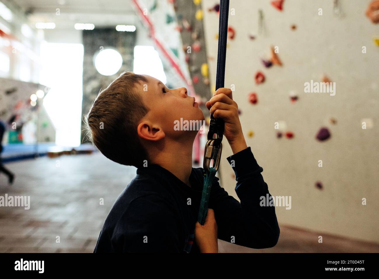 child holding onto a climbing rope ready to climb a wall indoors Stock Photo
