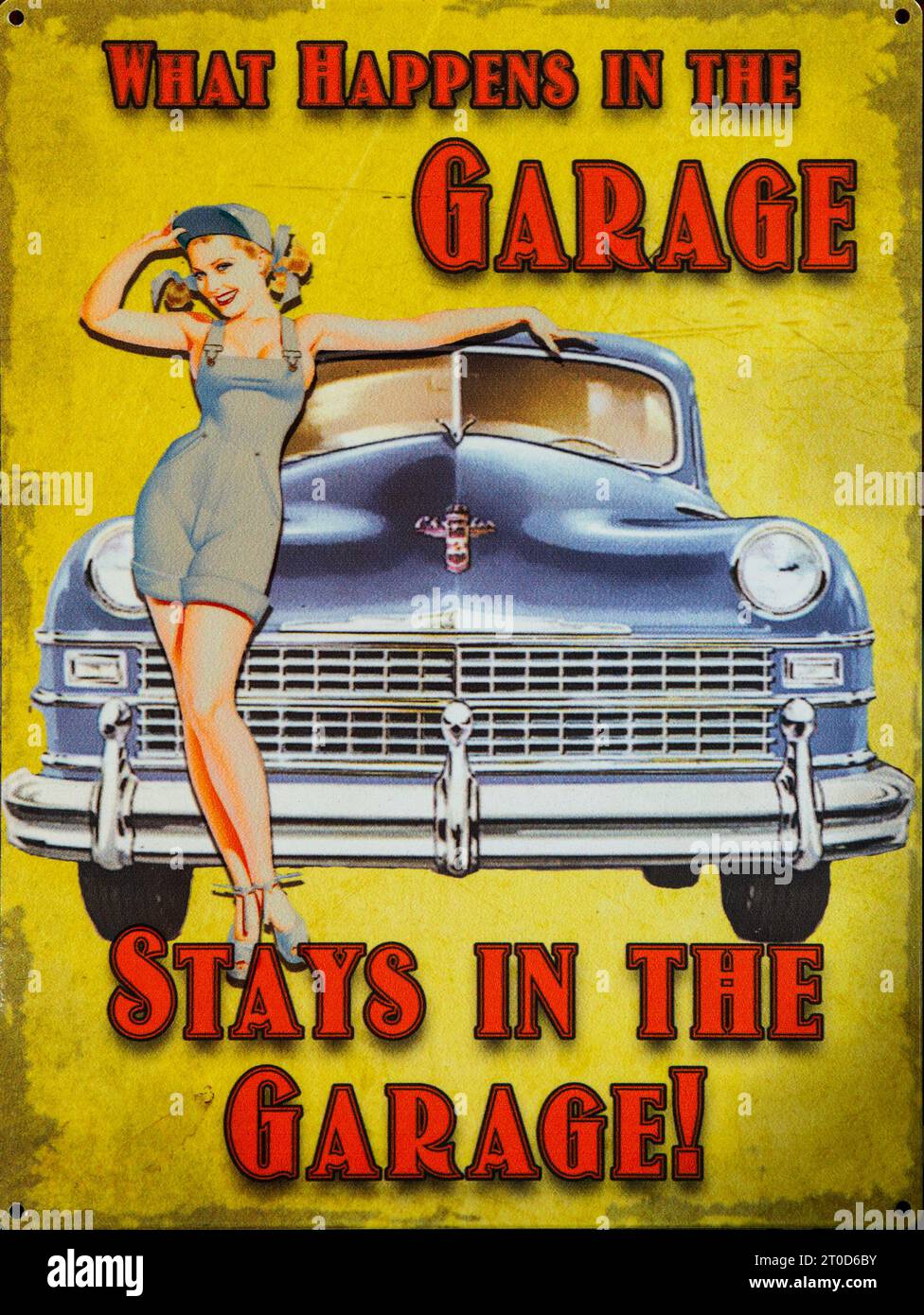 Old enamel sign 'What happens in the garage stays in the garage' woman posing by car Stock Photo