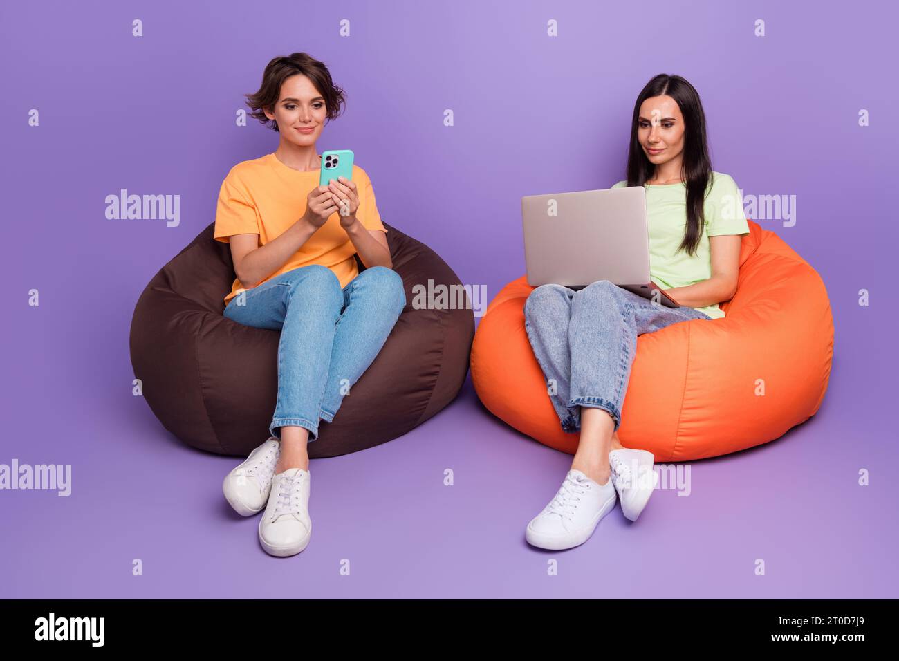 Full body photo of two colleagues cooperation together zone vip soft beanbags using netbook chat iphone isolated on purple color background Stock Photo