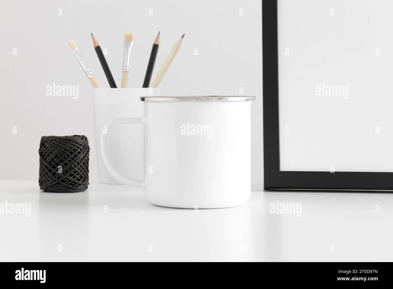 Enamel mug mockup with workspace accessories on a white table. Stock Photo